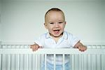 Baby standing in crib, smiling at camera