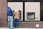 Thief looking over womans shoulder at cash machine