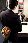 Männlichen Büroangestellten versteckt Blumen für Kollegin