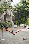 Businessman in garden jumping over barrier