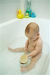 Baby taking bath, holding bath brush, full length