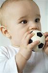 Baby putting toy soccer ball in mouth, close-up