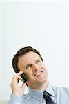 Businessman using cell phone, smiling, looking up, portrait