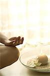 Female sitting in lotus position next to candle, cropped view of hand on bare knee