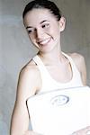 Young woman holding bathroom scale, smiling, portrait