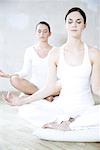 Two young women sitting in lotus position, eyes closed