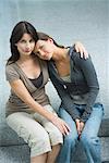 Mother and teenage girl sitting side by side, teen girl resting head on woman's shoulder