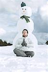 Young man meditating in front of snowman