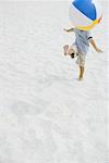 Boy kicking beach ball on beach, head hidden by ball, high angle view, full length