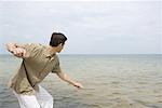 Man poised to skim stone on surface of ocean, side view, three quarter length