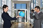 Businessman looking through field glasses to businesswoman holding a globe