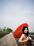 Woman standing on stone bridge outdoors with red parasol