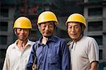 Three male construction workers with helmets outdoors smiling