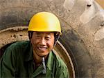 Construction worker sitting on tire of large machine smiling