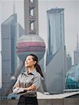 Businesswoman smiling outdoors with arms crossed and city skyline in background