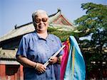 Woman standing outdoors with fabric on sticks with pagoda in background smiling