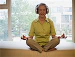 Reife Frau sitzen cross-legged meditieren mit Kopfhörer lächelnd