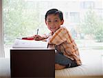 Boy sitting with workbook in front of large window smiling