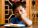 Boy sitting at table looking at plate with ambivalence