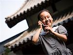 Girl standing outdoors with cell phone in front of pagoda smiling