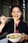 Woman with bowl of noodles and chopsticks smiling