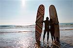 Couple with surfboards standing on beach.