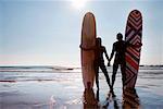 Couple standing on beach with surfboards holding hands.