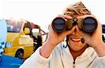 Man on beach with binoculars smiling with woman unloading van at the beach .