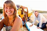 Woman on the beach smiling with couple waxing surfboards in background.