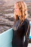 Woman standing with surfboard smiling .
