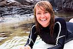 Woman lying on surfboard in the water laughing.