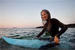 Woman sitting on surfboard in the water smiling.