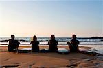 Four people sitting on the beach with surfboards.