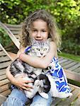 Young girl outdoors smiling with a cat on her lap.
