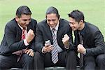 Three businessmen looking at a mobile phone and smiling