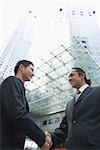 Low angle view of two businessmen shaking hands and smiling, Singapore