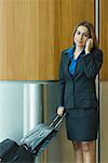 Portrait of a businesswoman talking on a mobile phone and holding her luggage