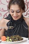Close-up of a young woman eating food with chopsticks and smiling