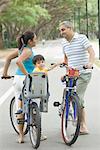 Profil de côté d'un couple adult mid parler les uns aux autres avec leur fils un vélo