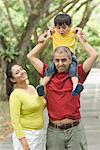 Mid adult man carrying his son on his shoulder with his wife standing beside him