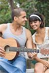 Young man sitting with his girlfriend and playing a guitar