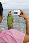 Rear view of a mid adult woman taking a photograph of a mid adult man on the beach