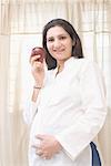 Portrait of a pregnant woman holding an apple and smiling