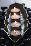 Gros plan de quatre bougies d'aromathérapie brûlant dans un plateau de galets noirs
