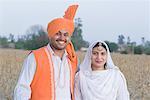 Portrait of a young couple standing in a wheat field and smiling