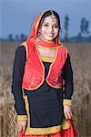 Portrait d'une jeune femme debout dans un champ de blé et souriant