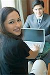 Portrait of a businesswoman using a laptop in front of a businessman in a hotel