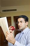 Close-up of a businessman reading a newspaper and eating an apple