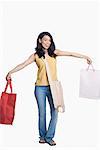 Portrait d'une jeune femme tenant des sacs à provisions avec ses bras tendus