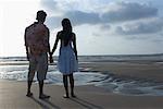Vue arrière d'un jeune couple avec main dans la main, debout sur la plage